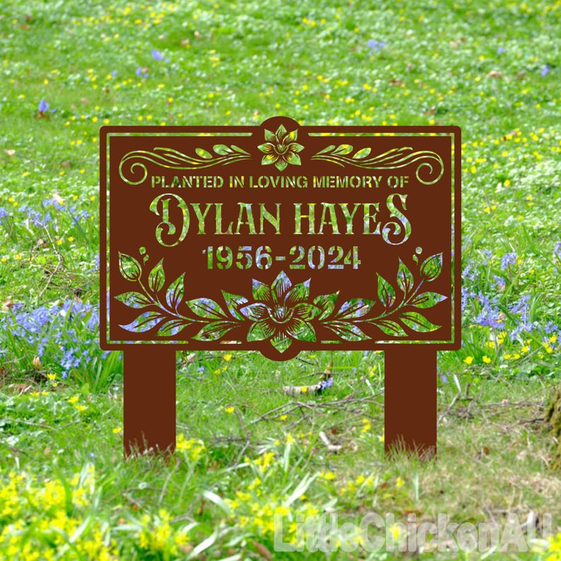 May include: A brown metal garden sign with a floral design and the text "Planted in loving memory of Dylan Hayes 1956-2024".