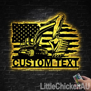 Puede incluir: Arte de pared de metal iluminado amarillo con la silueta de una excavadora sobre un diseño de bandera estadounidense. El texto "CUSTOM TEXT" se muestra debajo de la excavadora.