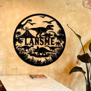 May include: Black metal wall decor featuring a circle with a dinosaur theme. The circle includes a variety of dinosaurs, a volcano, and palm trees. The name "LANSME" is written in large letters across the center of the circle.