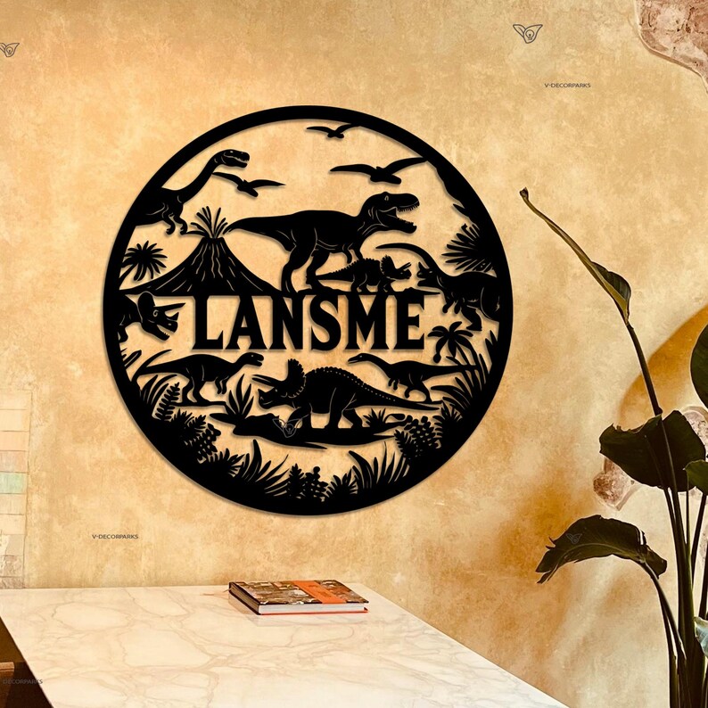 May include: Black metal wall decor featuring a circle with a dinosaur theme. The circle includes a variety of dinosaurs, a volcano, and palm trees. The name "LANSME" is written in large letters across the center of the circle.