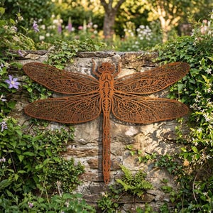 May include: A large, rusty-brown metal dragonfly wall art piece. The dragonfly has intricate cut-out wing designs and is mounted on a stone wall covered in greenery. The wingspan appears to be approximately 48 inches.