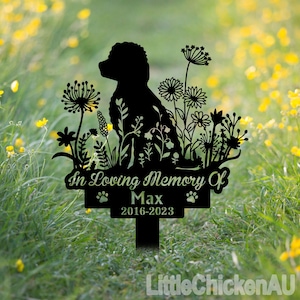 Puede incluir: Silueta negra de metal de un perro rodeado de flores con el texto "In Loving Memory Of Max 2016-2023" en un letrero. La silueta está sobre un fondo de hierba verde.
