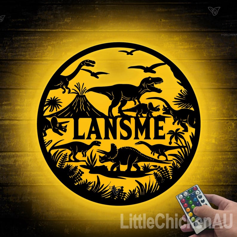 May include: A black metal circle with a dinosaur theme. The circle has a silhouette of a volcano, a T-Rex, a Triceratops, and other dinosaurs. The name "LANSMEN" is written in the center of the circle. The circle is illuminated with a yellow light.