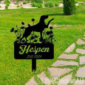 May include: Black metal silhouette of a dog standing in a field of flowers with the name "Hesper" and the dates "2012-2024" on a sign.