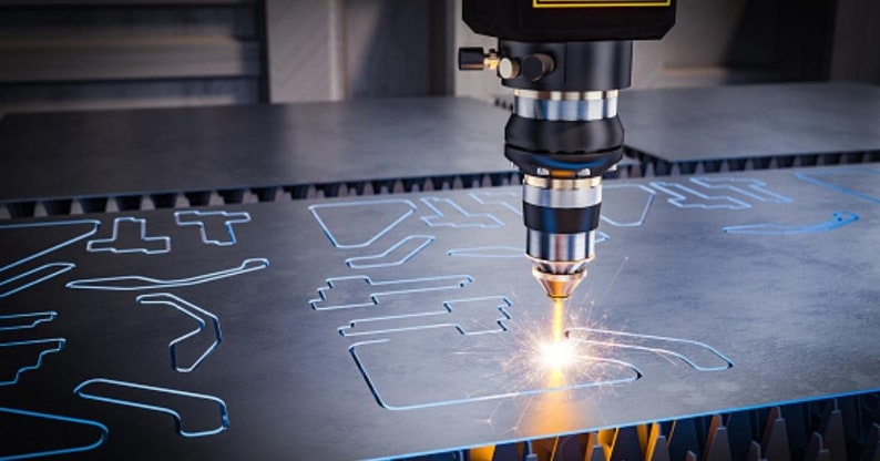 May include: A close-up of a laser cutter cutting a metal sheet. The laser beam is visible as a bright orange spark. The metal sheet has several cut-out shapes.