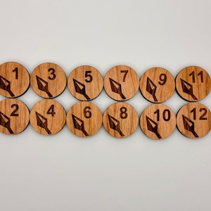 Könnte beinhalten: Zwölf hölzerne Spielsteine mit einem Speerdesign und den Zahlen 1 bis 12.