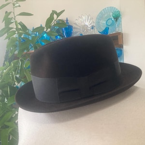May include: A dark brown fedora hat with a black band. The hat is displayed on a white mannequin head. The hat has a classic design, suitable for various occasions. The brim is approximately 6.35 cm wide.