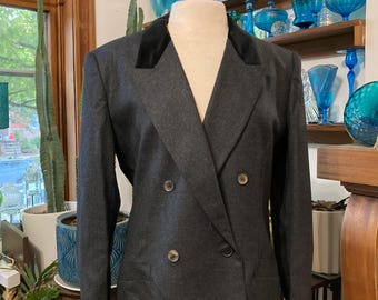 May include: A dark gray double-breasted blazer with a black velvet collar. The blazer has two rows of buttons and is displayed on a mannequin. The blazer is part of a clothing collection.