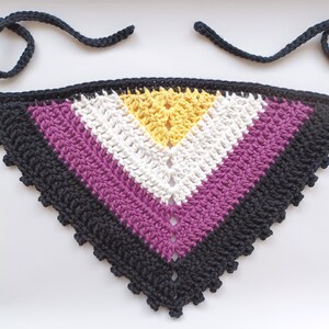 May include: A handmade crochet bandana in the non-binary pride flag colors. The bandana features a black border and ties, with stripes of black, purple, white, and yellow. The triangular shape is designed to be worn around the neck.