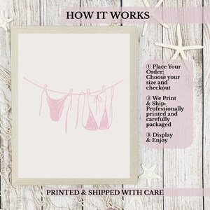 May include: A framed print featuring a pink line drawing of two bikinis hanging on a clothesline. The text "HOW IT WORKS" is at the top, and "PRINTED & SHIPPED WITH CARE" is at the bottom. The background is a light wood texture.