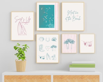 May include: A collection of framed art prints with a beach theme. The prints feature illustrations of surfboards, palm trees, and beach scenes. The color palette includes shades of pink, blue, and white. The text "Surf's Up Cowgirl" and "Meet me at the Beach" are visible.