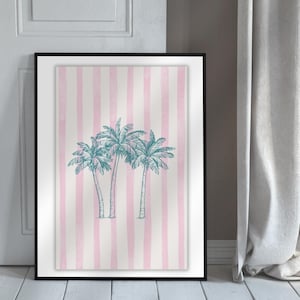 May include: A framed art print featuring a pink and white striped background with three teal palm trees. The artwork is displayed in a black frame and leans against a white door and a gray curtain.