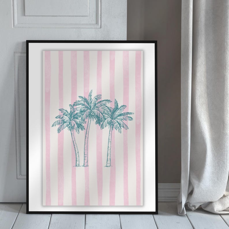 May include: A framed art print featuring a pink and white striped background with three teal palm trees. The artwork is displayed in a black frame and leans against a white door and a gray curtain.