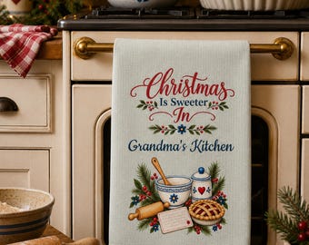 May include: A light-colored kitchen towel featuring the red and blue text 'Christmas Is Sweeter In Grandma's Kitchen' above an illustration of a mixing bowl, a wooden rolling pin, a lidded jar with a heart, and a pie surrounded by holly.