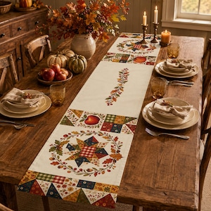 May include: A rectangular cream-colored table runner featuring a central vertical vine motif, flanked by repeating patterns of colorful patchwork stars, autumn leaves, acorns, and red apples, laid out on a rustic wooden dining table with place settings.
