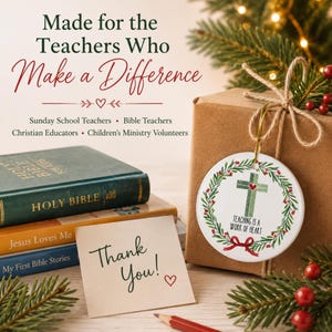 May include: A round white ceramic ornament featuring a green plaid cross, a red heart, and a wreath of holly leaves with the text "Teaching is a Work of Heart". The ornament is tied with a gold string to a brown gift box next to a stack of Bibles.