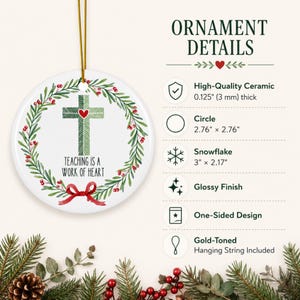 May include: A round white ceramic ornament with a gold-toned hanging string. The design features a green cross with a red heart, surrounded by a wreath of green leaves and red berries, with the text Teaching is a work of heart and a red bow.