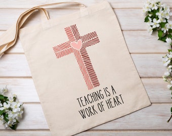 May include: A beige tote bag with a pink and brown cross design and the text "Teaching is a work of heart".