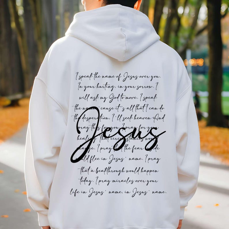 May include: White hoodie with a black text design that reads "I speak the name of Jesus over you. In your hurting, in your sorrow. I will ask my God to move. I speak the name... cause it's all that I can do the desperation. I'll seek heaven and pray this for you. I pray for you healing that circumstances were change. I pray the fear... would flee in Jesus' name. I pray that a breakthrough would happen today. I pray miracles over your life in Jesus' name, in Jesus' name."