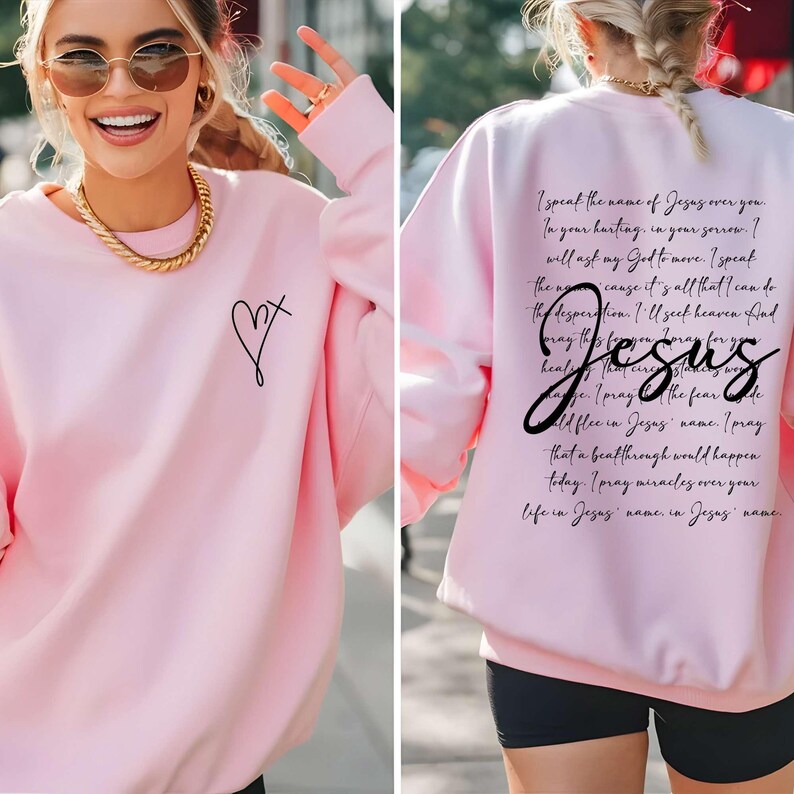 May include: Pink sweatshirt with a heart and cross design on the front and a religious message on the back. The message includes the word "Jesus" in large, bold letters.