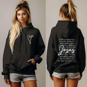 May include: Black hoodie with a white heart and cross on the front and a white text design on the back that reads "I speak the name of Jesus over you, for your healing in your season. I will last my God, I moved I spread the word, my God, I'll spread it. There is change, it's all I know, I'm living Jesus, I know I'm blind, but I'm loving the fear, that a faithful thing would happen. Today I pray miracles over you, your life in Jesus, name is Jesus, name."