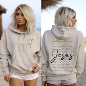 May include: A light beige hoodie with a small heart and cross design on the front. The back of the hoodie has a black print of a prayer in cursive writing that includes the word "Jesus".