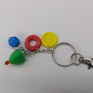 May include: A colorful keychain featuring a blue geometric bead, a red ring, and a yellow disc. A green cone-shaped charm with red accents is also attached. The keychain has a silver chain and a clasp.