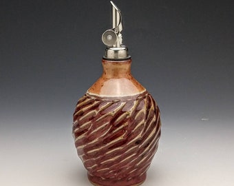 May include: A ceramic olive oil bottle with a swirl design in shades of brown and red. The bottle has a silver metal pour spout.