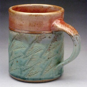 May include: A ceramic mug with a light green glaze and a red rim. The mug has a textured design of small triangles and a handle.