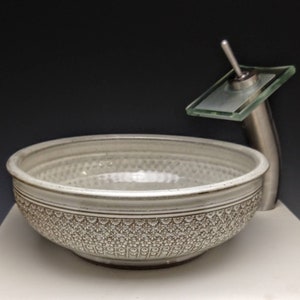 Può includere: Un lavandino in ceramica bianca con un motivo decorativo attorno al bordo. Un rubinetto cromato con un becco in vetro è attaccato al lato del lavandino.