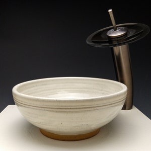 Può includere: Un lavabo da bagno in ceramica bianca con un bordo marrone e un rubinetto in nichel spazzolato con un becco nero.