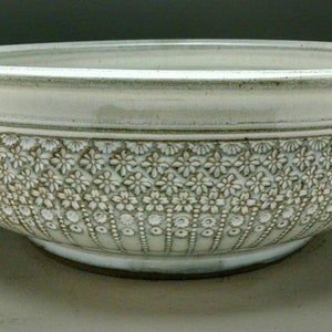 May include: A white ceramic bowl with a decorative floral pattern around the rim. The bowl is slightly wider at the top and tapers down to a rounded base.