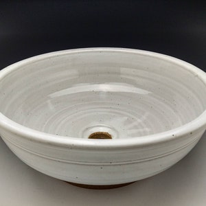 May include: White ceramic sink with a round shape and a drain hole in the center. The sink has a smooth, glazed finish and a slightly textured rim.