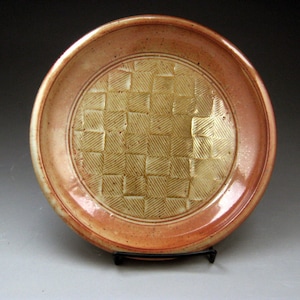 Può includere: Un piatto in ceramica con una glassa marrone chiaro e un design testurizzato. Il piatto ha un bordo rosso.