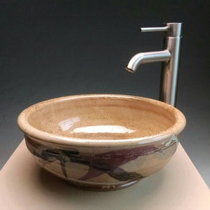 May include: A ceramic vessel sink with a brown glaze and abstract red and white painted designs. The sink is paired with a brushed nickel faucet.