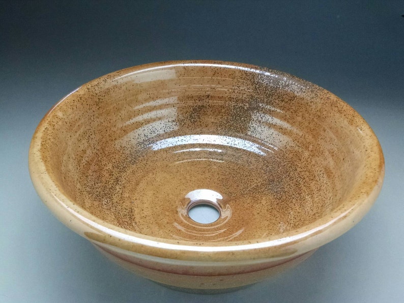 May include: A brown ceramic sink with a speckled glaze and a white rim. The sink has a round shape and a small drain hole in the center.