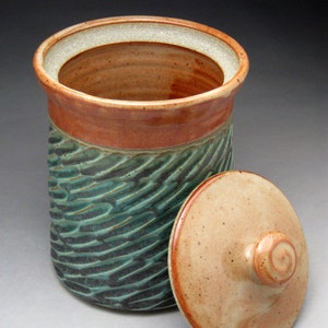 May include: A ceramic jar with a lid, featuring a green and brown swirl pattern. The jar has a wide mouth and a rounded shape.