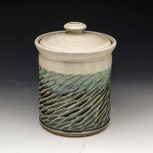 May include: A white ceramic jar with a lid, featuring a green and blue glaze with a textured pattern. The jar is perfect for storing dry goods like sugar, flour, or coffee.