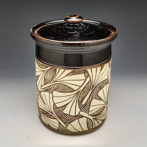 May include: A ceramic storage jar with a lid, featuring a white background with a brown ginkgo leaf pattern.