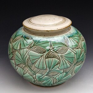 Può includere: Un vaso in ceramica con coperchio, decorato con un motivo a foglie di ginkgo verde e bianco.