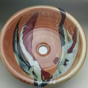 May include: A ceramic sink with a brown, red, and black glaze. The sink has a round shape and a single drain hole in the center.