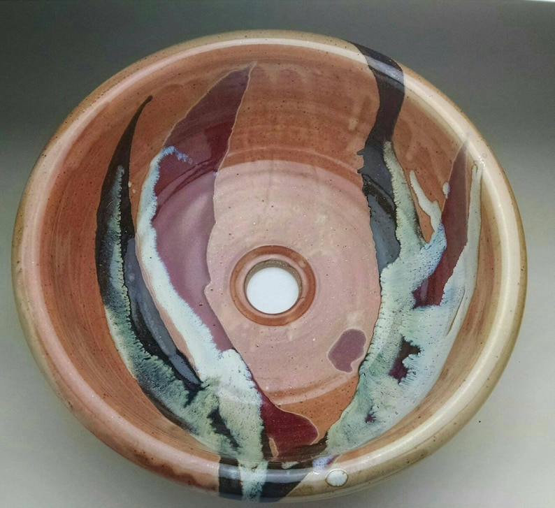 May include: A ceramic sink with a brown, red, and black glaze. The sink has a round shape and a single drain hole in the center.