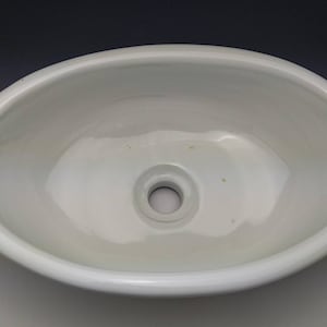 Può includere: Lavandino ovale in ceramica bianca con un foro di scarico rotondo al centro.