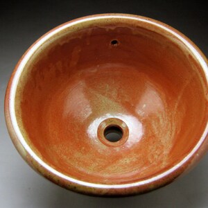 May include: A ceramic sink with a reddish-brown glaze and a white rim. The sink has a small drain hole in the center.