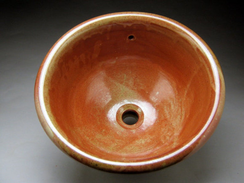 May include: A ceramic sink with a reddish-brown glaze and a white rim. The sink has a small drain hole in the center.