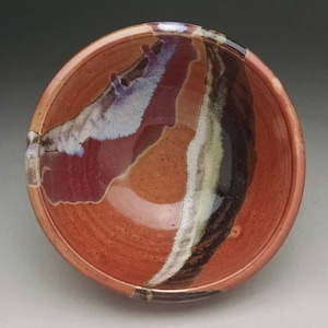 May include: A ceramic bowl with a red, brown, white, and black glaze. The bowl has a unique, abstract design.