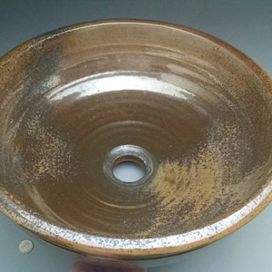 May include: A brown ceramic sink with a white glaze and a drain hole in the center. The sink has a speckled appearance and a slightly uneven surface.