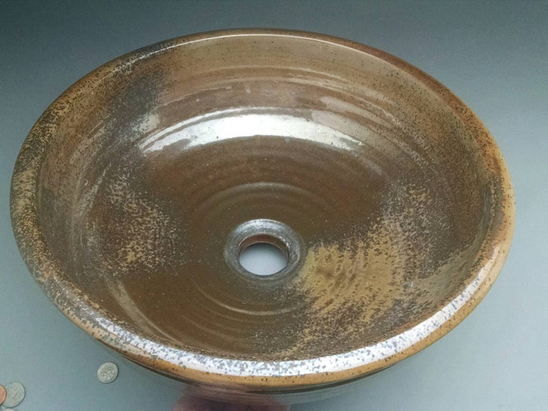 May include: A brown ceramic sink with a white glaze and a drain hole in the center. The sink has a speckled appearance and a slightly uneven surface.