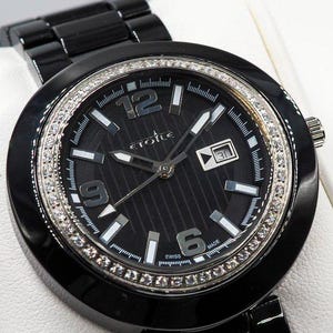 May include: A black ceramic wristwatch with a round case and a matching link bracelet. The black dial features silver-tone hands, hour markers, the text ETOILE, and a date window at the three o'clock position. A bezel set with clear stones surrounds the dial.