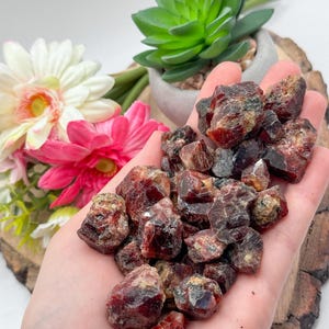 Puede incluir: Un puñado de cristales de granate en bruto de color rojo y marrón.